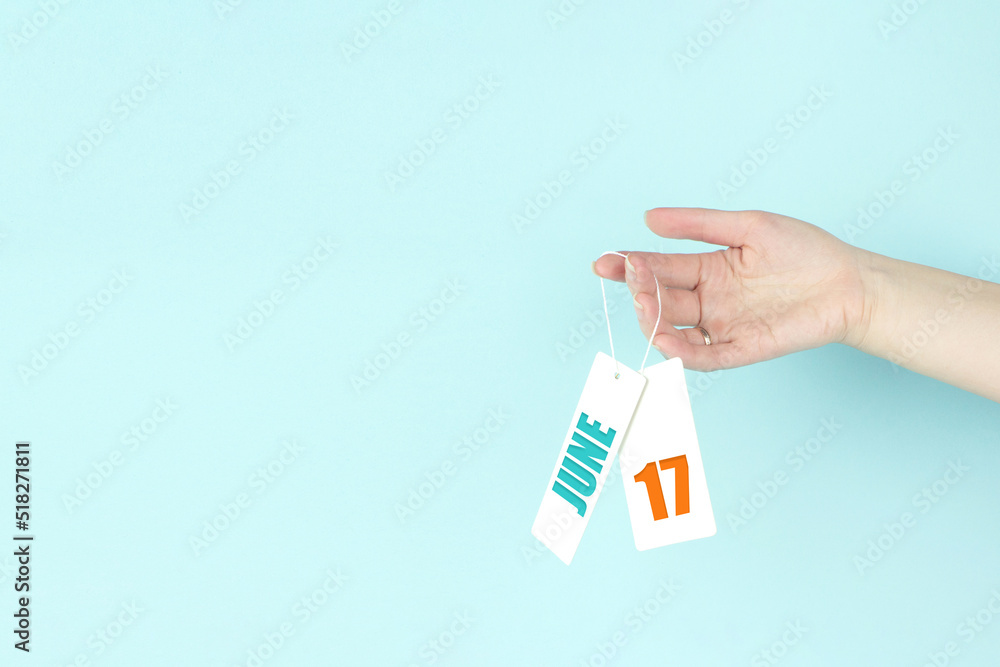 June 17th. Day 17 of month, Calendar date. Hand hold price tag with calendar date on blue background. Summer month, day of the year concept. June 17th. Day 17 of month, Calendar date. Hand hold price tag with calendar date on blue background. Summer month, day of the year concept.