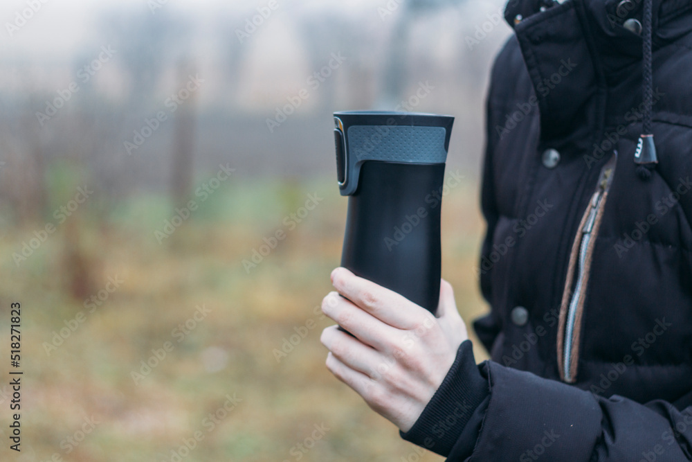 In late autumn, men's hands are warming themselves on a black toggle switch with a hot drink. Environmentally friendly use of reusable glasses, mugs. Rejection of plastic In late autumn, men's hands are warming themselves on a black toggle switch with a hot drink. Environmentally friendly use of reusable glasses, mugs. Rejection of plastic