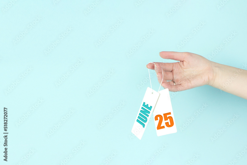 June 25th. Day 25 of month, Calendar date. Hand hold price tag with calendar date on blue background. Summer month, day of the year concept. June 25th. Day 25 of month, Calendar date. Hand hold price tag with calendar date on blue background. Summer month, day of the year concept.