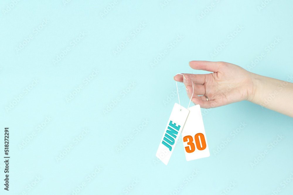 June 30th. Day 30 of month, Calendar date. Hand hold price tag with calendar date on blue background. Summer month, day of the year concept. June 30th. Day 30 of month, Calendar date. Hand hold price tag with calendar date on blue background. Summer month, day of the year concept.