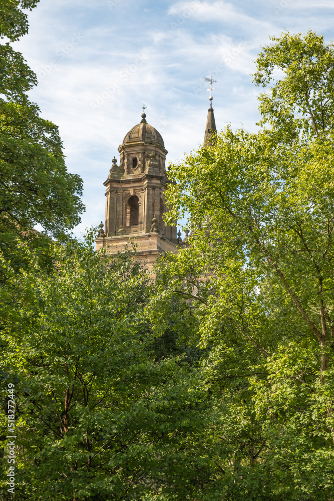 Ancient and historic church spire behind lush green trees on a bright and sunny day