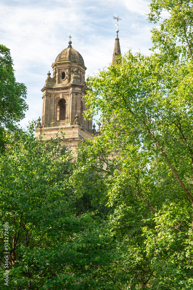 Ancient and historic church spire behind lush green trees on a bright and sunny day