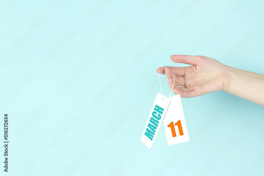 March 11st . Day 11 of month, Calendar date. Hand hold price tag with calendar date on blue background. Spring month, day of the year concept. March 11st . Day 11 of month, Calendar date. Hand hold price tag with calendar date on blue background. Spring month, day of the year concept.