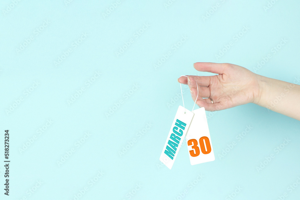 March 30th. Day 30 of month, Calendar date. Hand hold price tag with calendar date on blue background. Spring month, day of the year concept. March 30th. Day 30 of month, Calendar date. Hand hold price tag with calendar date on blue background. Spring month, day of the year concept.
