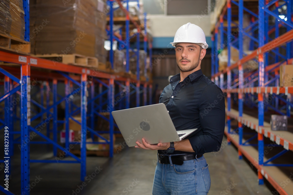 Young caucasian male worker wearing helmet using laptop in modern warehouse. Young caucasian male worker wearing helmet using laptop in modern warehouse.
