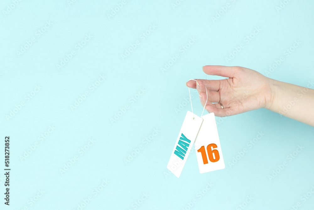 May 16th. Day 16 of month, Calendar date. Hand hold price tag with calendar date on blue background. Spring month, day of the year concept. May 16th. Day 16 of month, Calendar date. Hand hold price tag with calendar date on blue background. Spring month, day of the year concept.