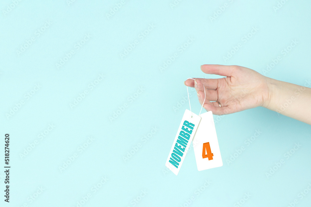 November 4th. Day 4 of month, Calendar date. Hand hold price tag with calendar date on blue background. Autumn month, day of the year concept. November 4th. Day 4 of month, Calendar date. Hand hold price tag with calendar date on blue background. Autumn month, day of the year concept.