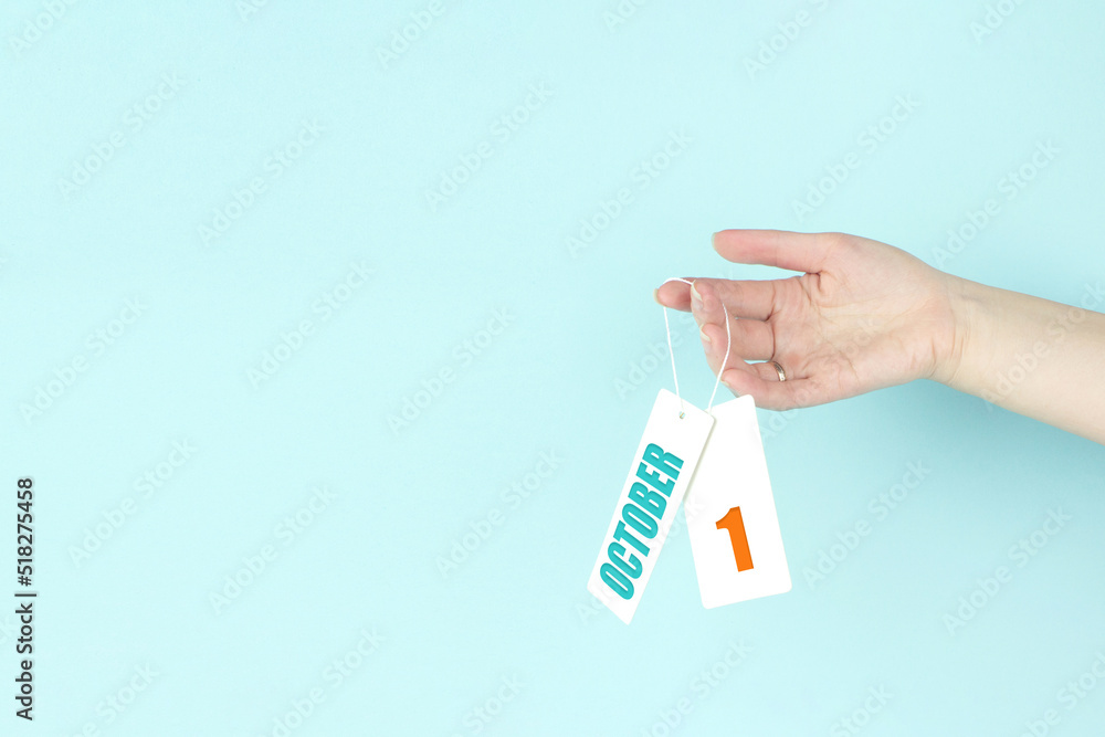 October 1st . Day 1 of month, Calendar date. Hand hold price tag with calendar date on blue background. Autumn month, day of the year concept. October 1st . Day 1 of month, Calendar date. Hand hold price tag with calendar date on blue background. Autumn month, day of the year concept.