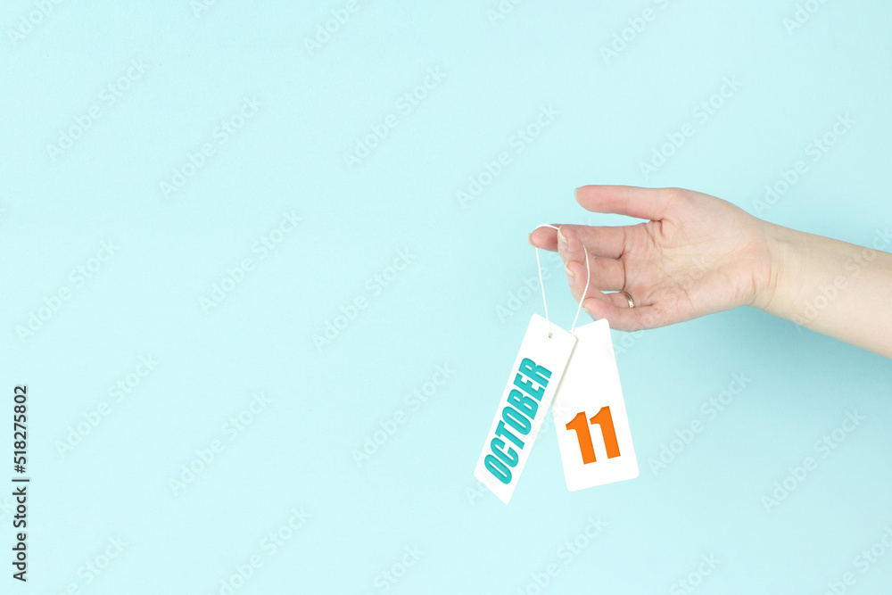 October 11st . Day 11 of month, Calendar date. Hand hold price tag with calendar date on blue background. Autumn month, day of the year concept. October 11st . Day 11 of month, Calendar date. Hand hold price tag with calendar date on blue background. Autumn month, day of the year concept.