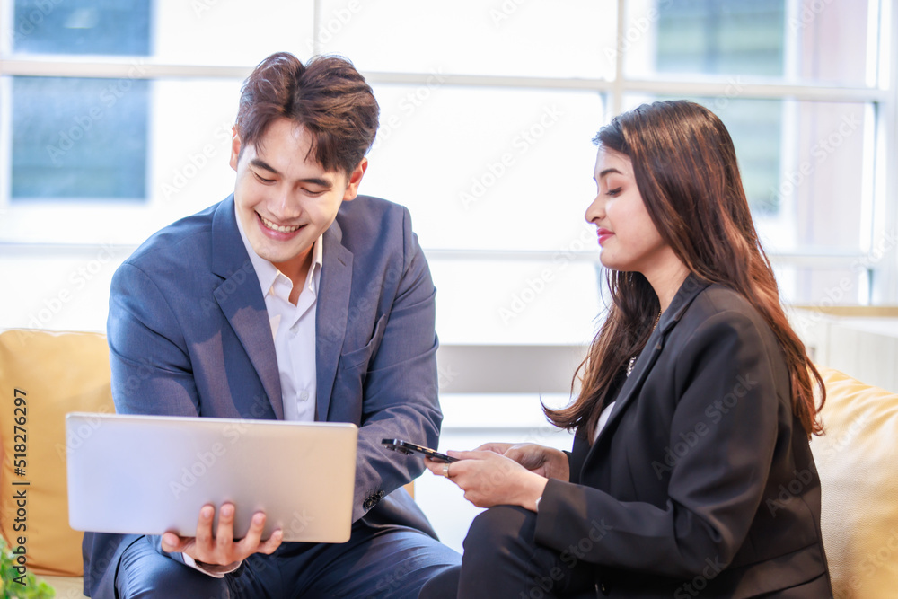 Millennial Asian professional successful male businessman and female businesswoman in formal suit sitting on sofa smiling discussing together while working with laptop notebook computer in office Millennial Asian professional successful male businessman and female businesswoman in formal suit sitting on sofa smiling discussing together while working with laptop notebook computer in office