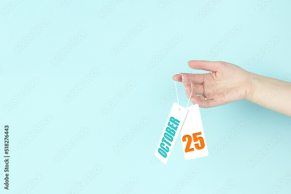 October 25th. Day 25 of month, Calendar date. Hand hold price tag with calendar date on blue background. Autumn month, day of the year concept. October 25th. Day 25 of month, Calendar date. Hand hold price tag with calendar date on blue background. Autumn month, day of the year concept.