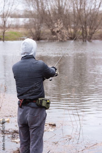 A geared up man fishing standing in the river or lake with a small fishing rod