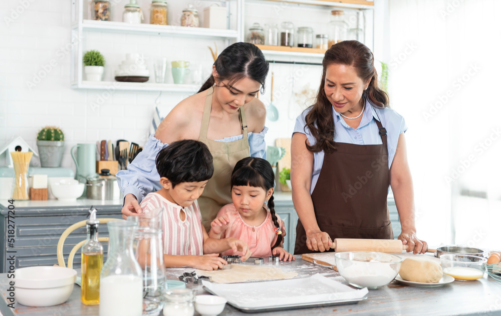 Happy Asian family making preparation dough and bake cookies in kitchen at home. Enjoy family activity together.