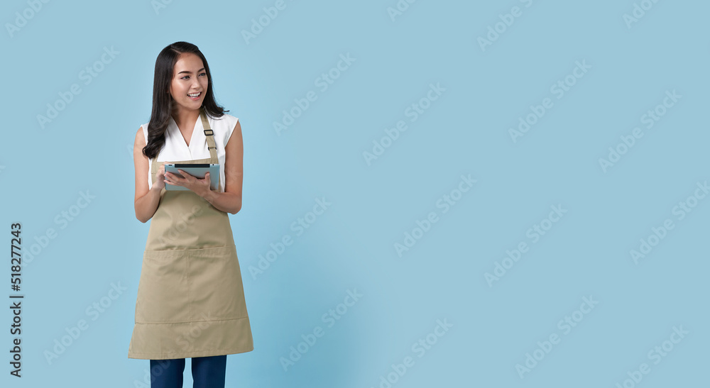 Young asian entrepreneur woman in apron hand holding tablet for list order food isolated on blue background. Barista and waitress service concept. Young asian entrepreneur woman in apron hand holding tablet for list order food isolated on blue background. Barista and waitress service concept.
