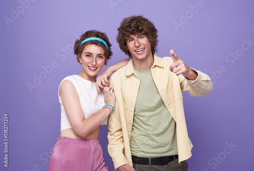 portrait of happy excited couple tourists pointing hands to front on isolated light purple background.