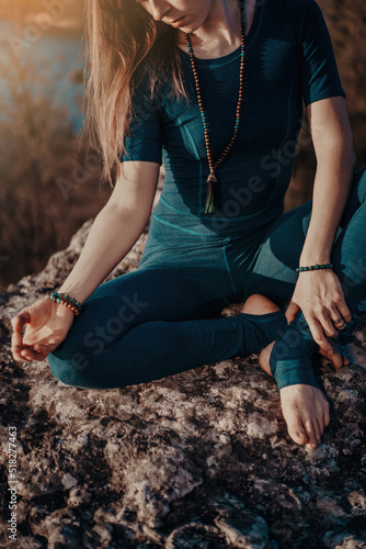 Yogi woman sitting in mala beads with gyan mudra, meditating, feeling free in front of wild nature. Mindful fitness coach having zen moment. Everyday yoga practice, calm breath, concentration