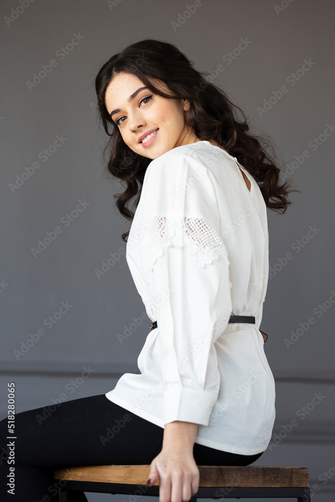Beautiful smiling young woman wear in a white shirt, looking at camera posing in a studio, isolated grey wall background.