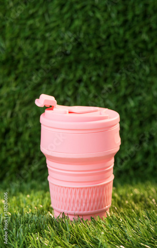 Modern pink collapsible silicone cup on the background of green nature. reusable thermos bottle. Go plastic free. No waste