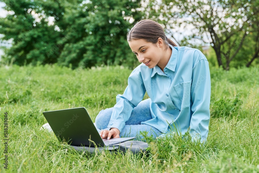 Teenage girl high school student using laptop while sitting on green grass Teenage girl high school student using laptop while sitting on green grass