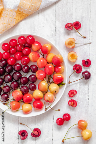 White plate with colorful cherries on a white background, Yellow and red cherries. Sweetfruit salad. Healthy eating concept. Top view. photo