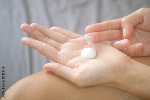 Asia woman sitting on bed and applying cream on her hand.