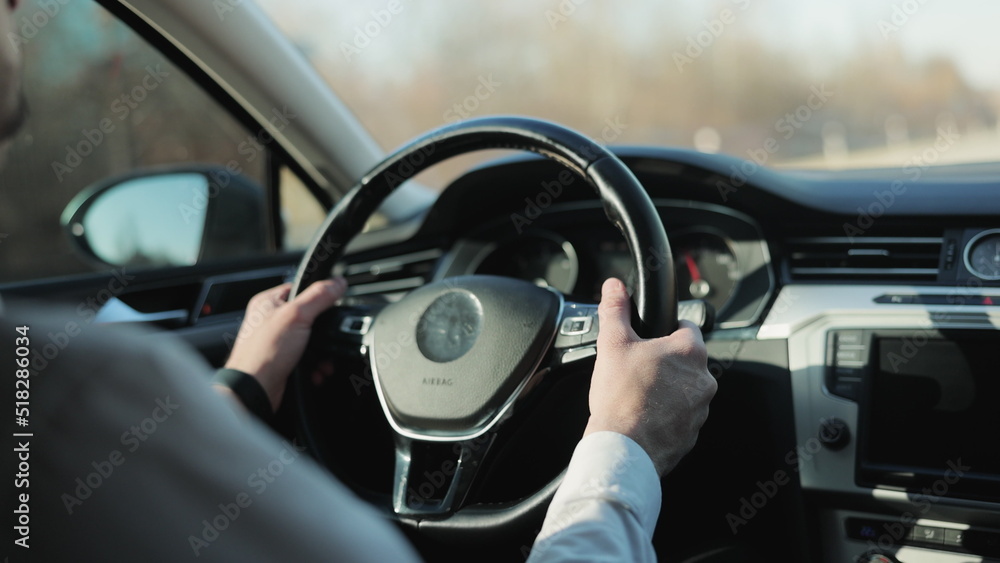 Man driving car with autopilot. Businessman in white shirt driving car. Driver's hand on the steering wheel against the background of the road. Elegant male driver traveling by automobile