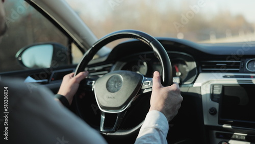Man driving car with autopilot. Businessman in white shirt driving car. Driver's hand on the steering wheel against the background of the road. Elegant male driver traveling by automobile