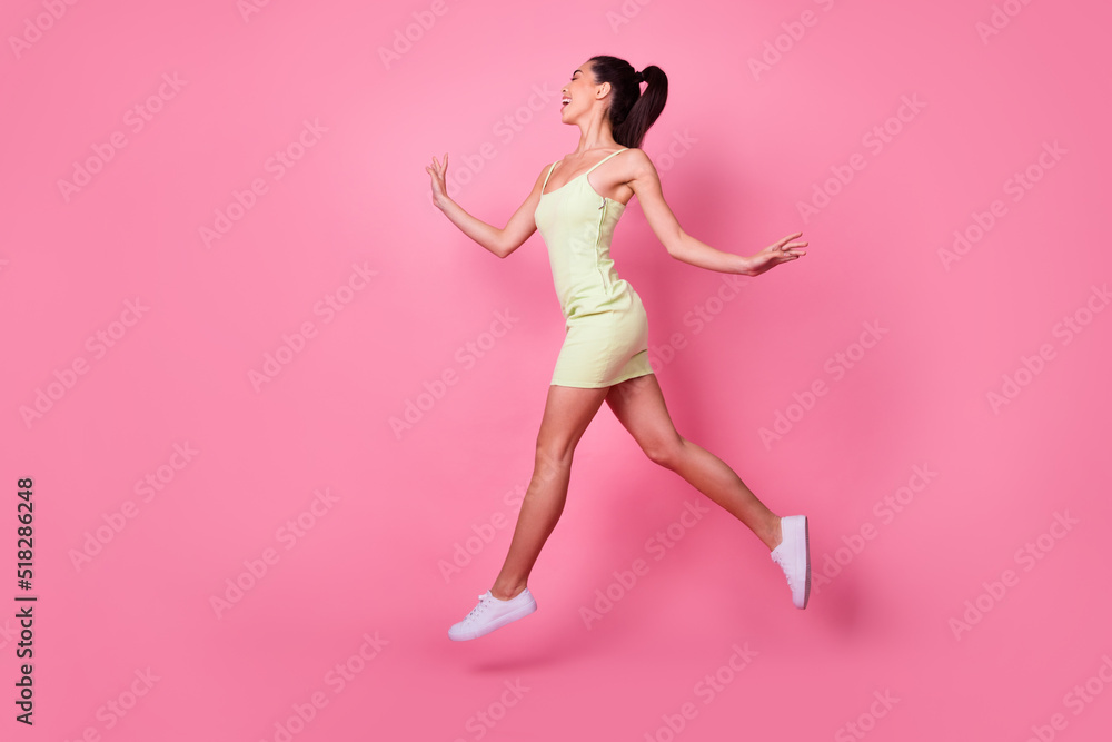 Full length photo of excited dreamy woman wear yellow dress jumping high looking empty space isolated pink color background