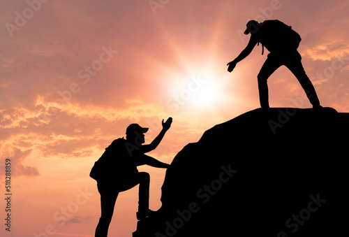 Silhouettes of people climbing on mountain at sunset. People helping and, team work concept.