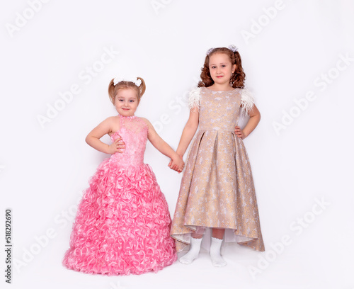 A pair of adorable little girls in ball gowns isolated on a white background. Full-length image
