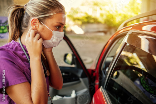 Nurse secures mask at her car in parking lot. A Caucasian young woman wearing uniform puts her mask into place. © Jelena Stanojkovic