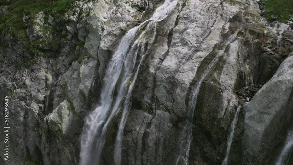 Aerial view close up flight with mountain waterfalls flowing from glacier over rocks. Fall of water in a green mountain gorge. Movement in three axes Aerial view close up flight with mountain waterfalls flowing from glacier over rocks. Fall of water in a green mountain gorge. Movement in three axes