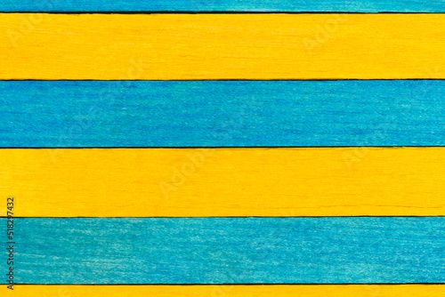 Blue and yellow painted wooden boards. Bright wooden textured background. A wall of alternating blue and yellow wooden boards arranged horizontally.