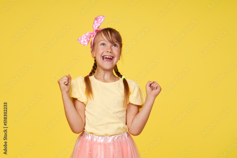 Portrait of surprised cute little toddler girl child over yellow background. Looking at camera. Points hands to the side. Advertising childrens products.