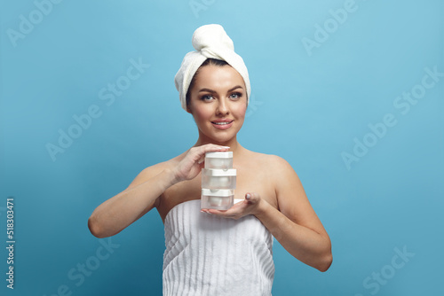 Attractive smiling woman with a pleasure facial and clean skin holds beauty products for rejuvenation and skin care on a blue isolated background.