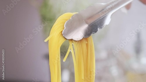 Taking spaghetti with kitchen tongs from saucepan.
