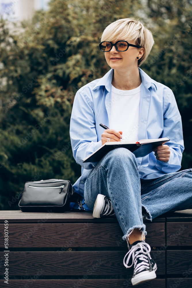 Obraz premium Young woman sitting on bench and writing in a notebook