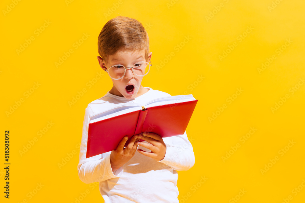Portrait of cute little boy, happy kid reading book isolated on bright yellow background with. Concept of child emotions, facial expression, fashion and ad. Portrait of cute little boy, happy kid reading book isolated on bright yellow background with. Concept of child emotions, facial expression, fashion and ad.