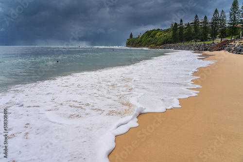 Low angled view of white foamy waves on a sandy beach with dark storm clouds on the horizon photo
