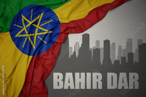 abstract silhouette of the city with text Bahir Dar near waving colorful national flag of ethiopia on a gray background. photo