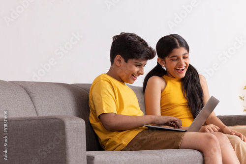 Boy and girl using laptop while sitting on sofa in living room