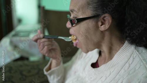 An older woman eating pasta sitting on couch