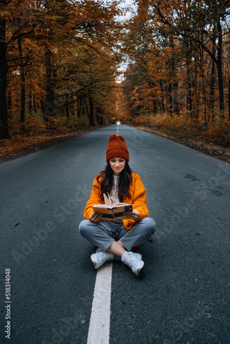 Confidence woman with book sitting on the road with autumn tree around. New life, path choice, ambition © irissca