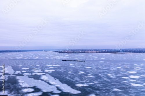 A cargo container ship moves along a frozen river. Freight transportation concept, import export and business logistics, aerial view in winter.