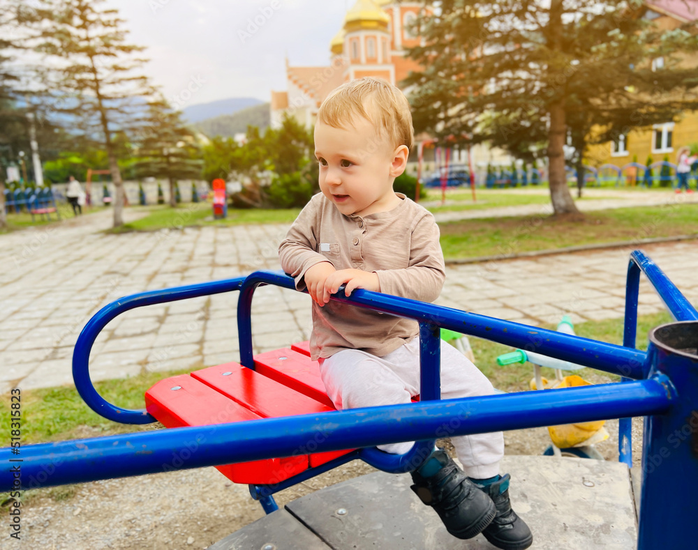 A cute boy of one and a half years rides on a swing in the playground. Children's entertainment. Selective focus