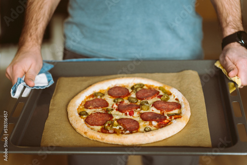 A man holds a baking sheet with pizza. Baking sheet covered with baking paper