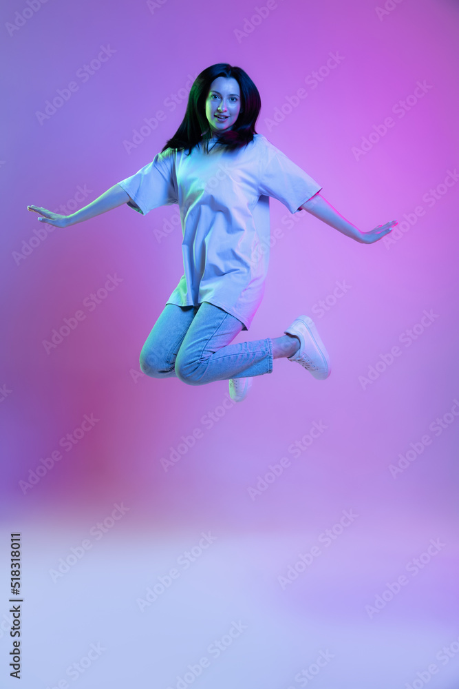 Portrait of adorable girl, young woman with long glossy dark hair isolated on purple background in neon light. Concept of beauty, art, fashion, emotions