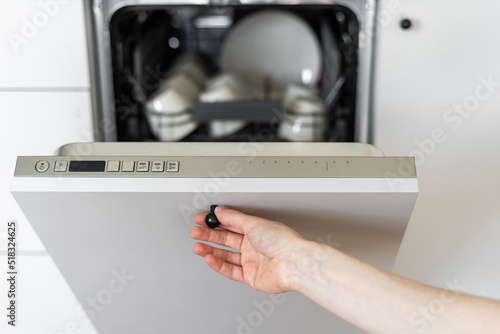 Woman's hand starting dishwasher with dirty utensils