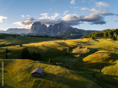 Aerial view of Seiser Alm plateau with traditional wooden mountain cottages on the meadows in Dolomites mountains in Italy. Morning drone shot of idyllic Alpe di Suisi blooming meadow in South Tyrol. 
