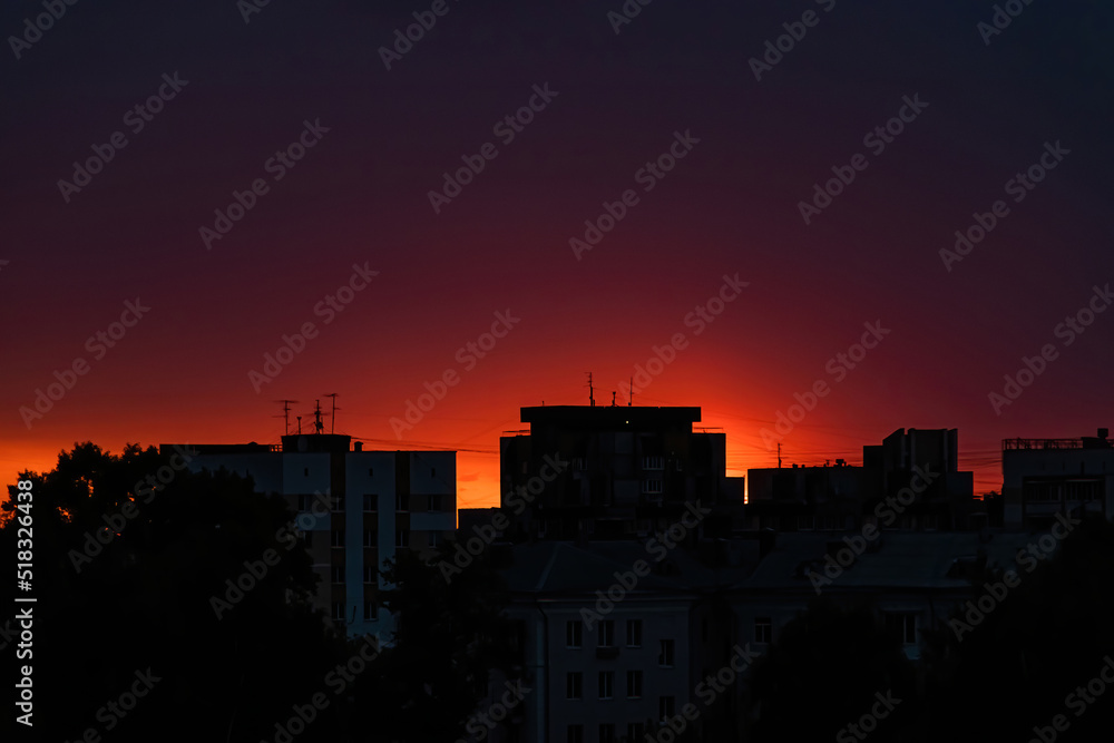 Silhouette of the city at sunset. Sun is rising over tall buildings.